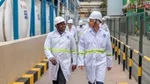 Two men in white lab coats and hard hats at an industrial facility.