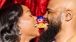 Smiling couple share a pastry while holding a small jar of Vaseline between their noses.