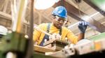 A man wearing a blue hard-hat, protective glasses and gloves working in a factory.