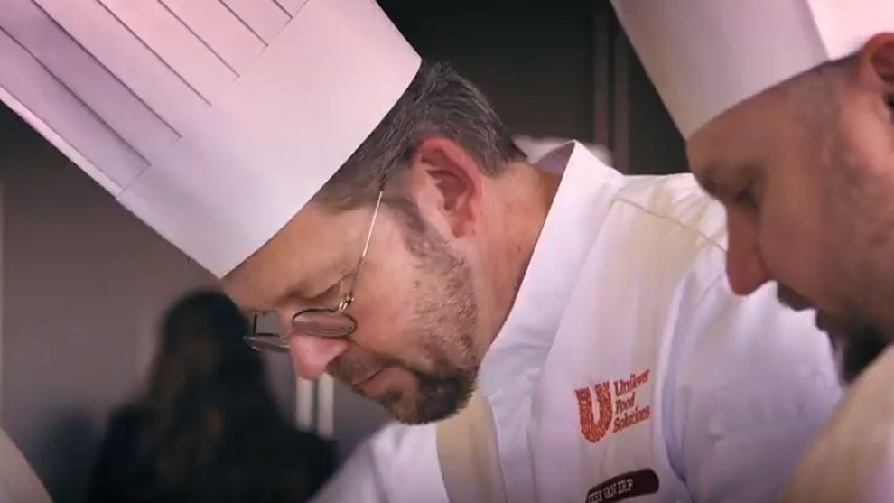 A man wearing glasses, a chefs hat and chef whites featuring the Unilever Food Solutions logo