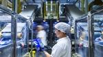A factory worker looks at some packaging. Factory machinery and factory workers are blurred in the background.