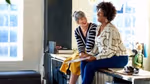 Two women sitting on a worktop chatting and laughing.