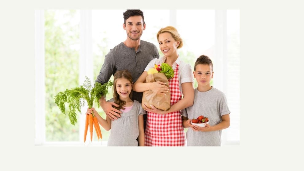 Family of mother and father with two children holding bag of groceries with fruits & vegetables