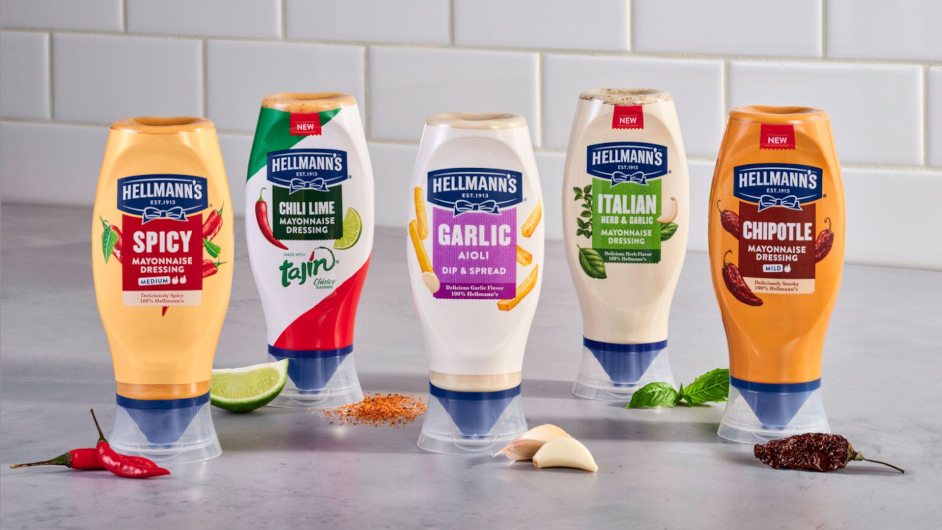 A line-up of Hellmann’s flavoured, squeeze bottle mayos pictured with key ingredients like limes, chillies, garlic and herbs.