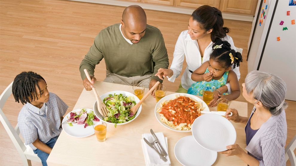 Mother & father serving two children dinner at table.