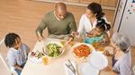 Mother & father serving two children dinner at table.