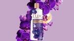 A bottle of Lux Magical Orchid lays on purple flowers on a violet background.