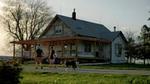 A man with a child on his shoulders, a woman, a small girl and a dog walk up to a farm house