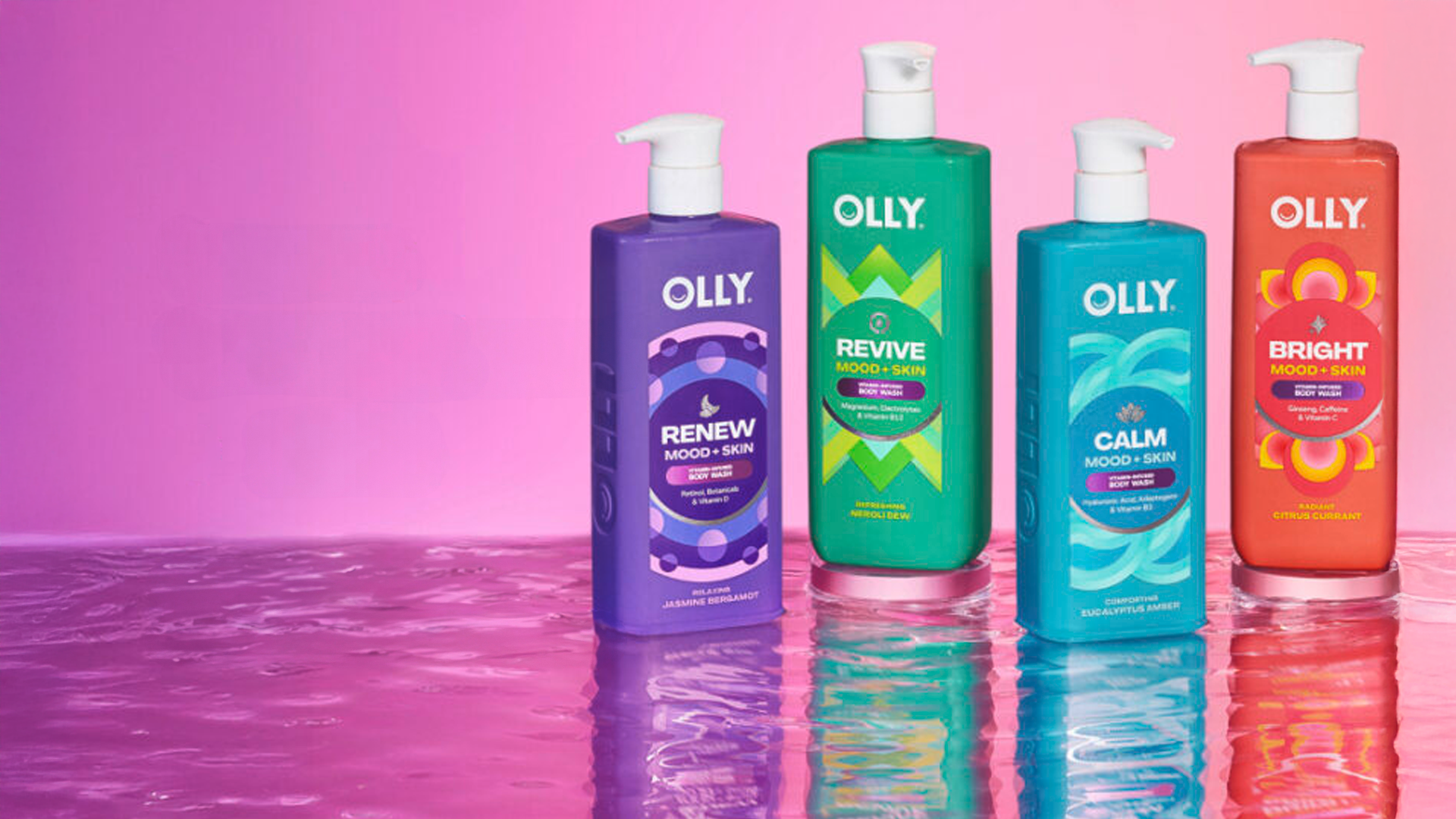 Four colourful Olly Mood + Skin body wash bottles stand on a reflective surface against a pink gradient background.