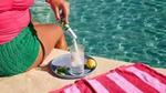 Lady sitting beside a swimming pool pouring Liquid I.V powdered hydration mix into a glass of water